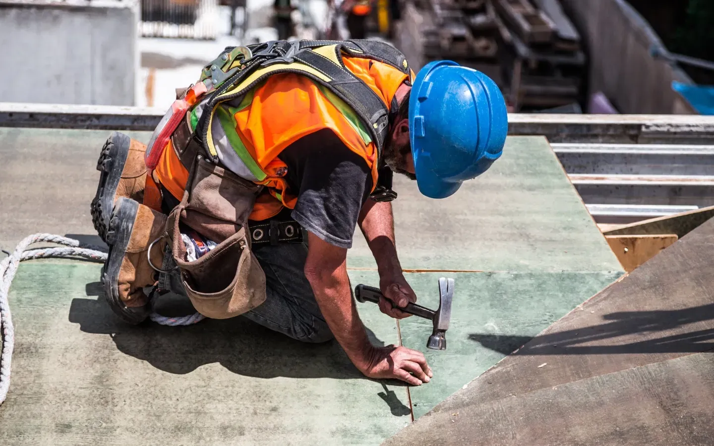 A construction worker is kneeling down on the ground while holding a hammer.