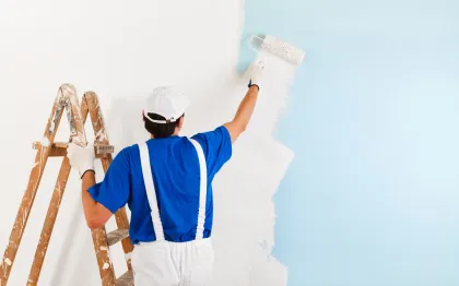 Israel Inc. - A man is painting a wall with a roller while standing on a ladder.