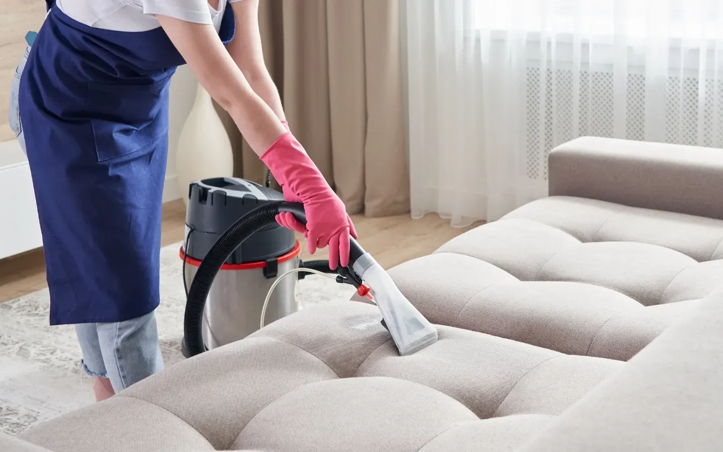 A woman is cleaning a couch with a vacuum cleaner.