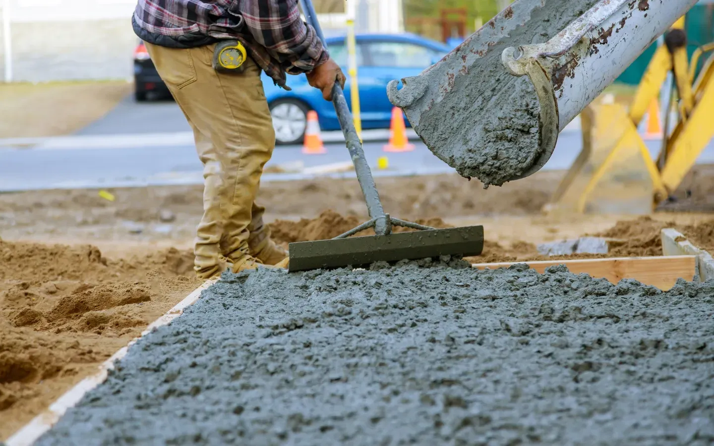 A man is spreading concrete on a sidewalk with a rake.