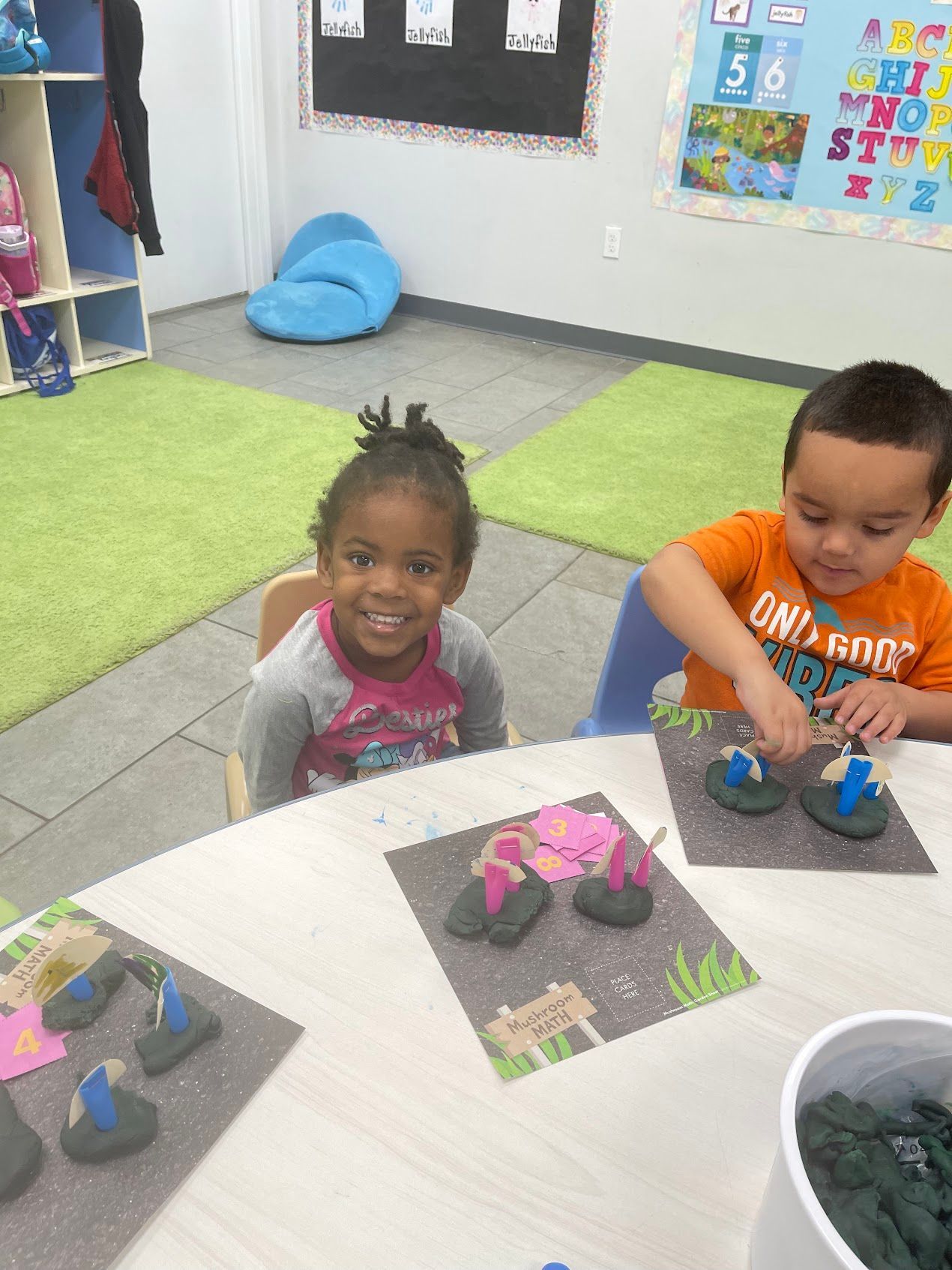 A boy and a girl are sitting at a table playing with clay.