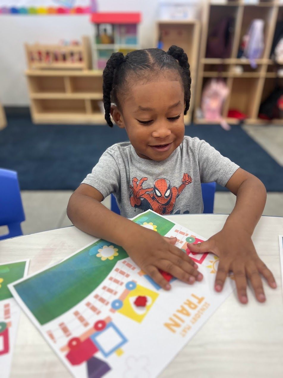 A little girl wearing a spider man shirt is sitting at a table