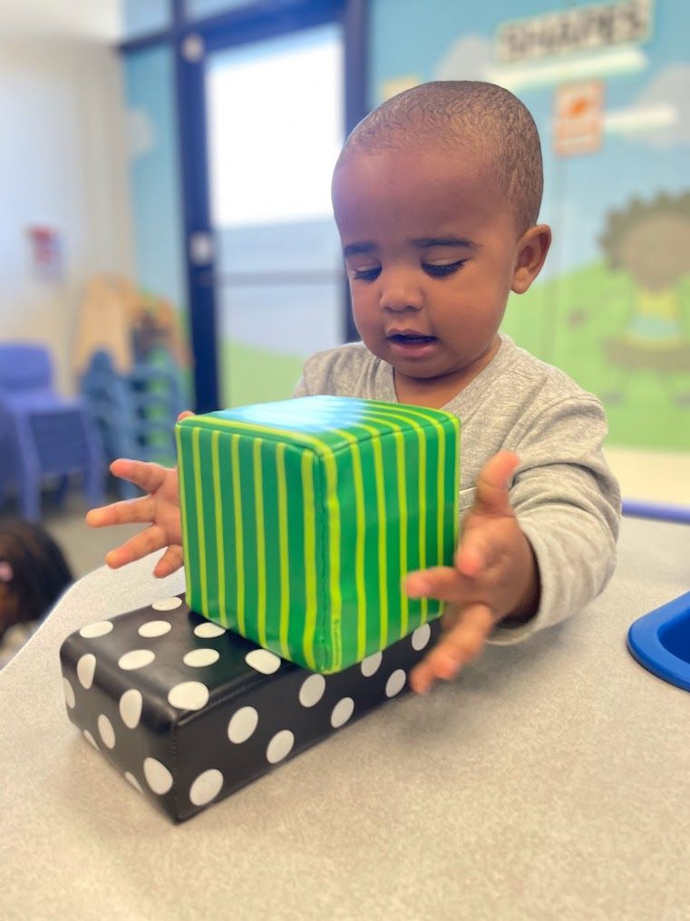 A young boy is playing with a green striped cube on top of a black and white polka dot box.