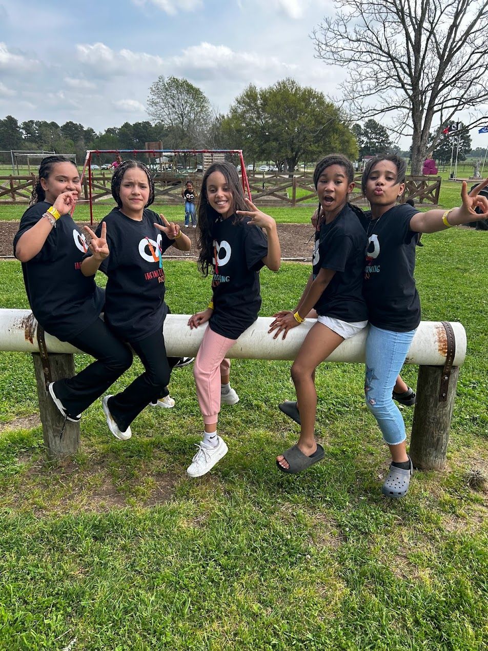 A group of young girls are sitting on a log in a park.