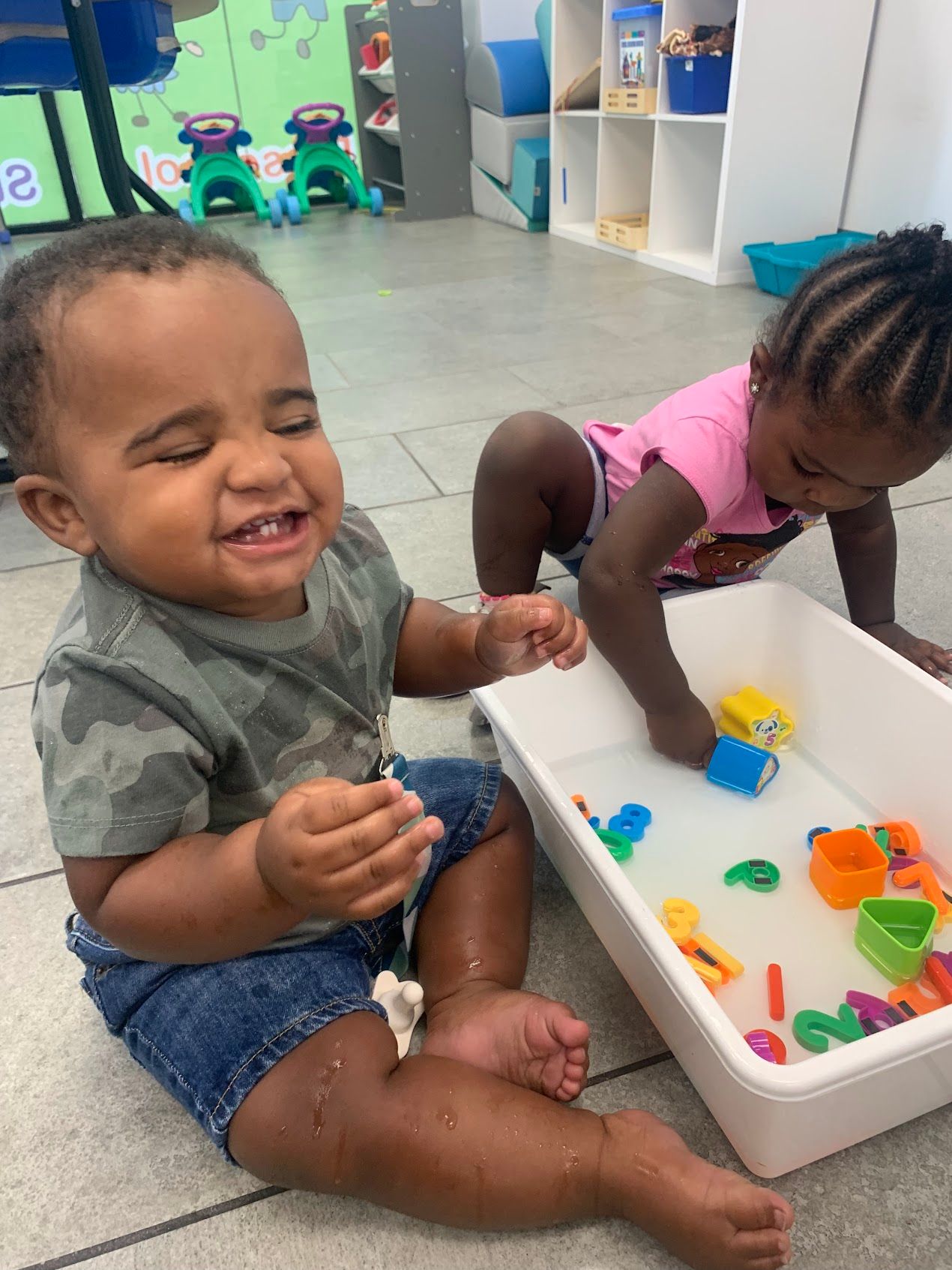 A boy and a girl are sitting on the floor playing with water toys.