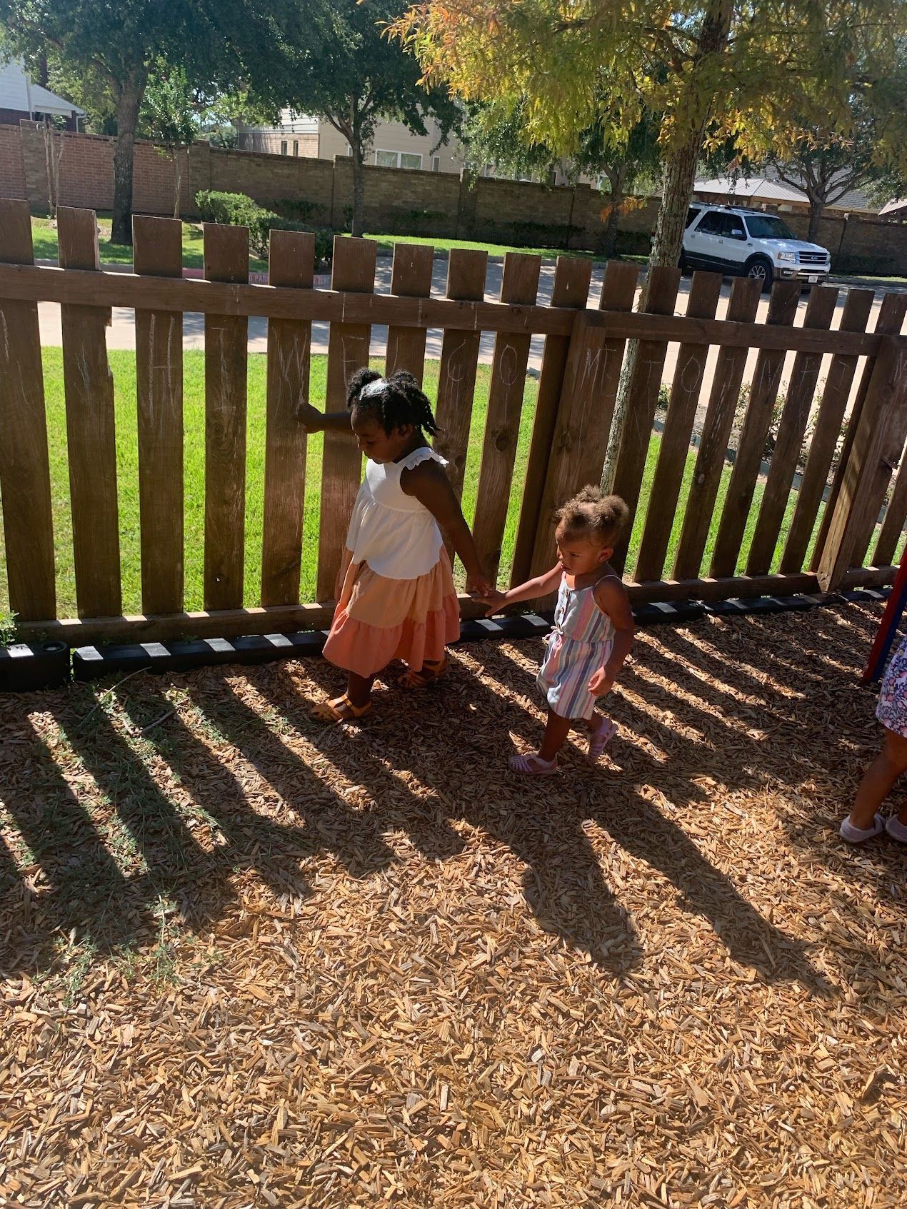 Two little girls are standing next to a wooden fence.