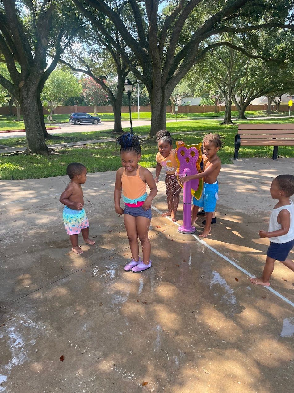 A group of children are playing in a sprinkler in a park.