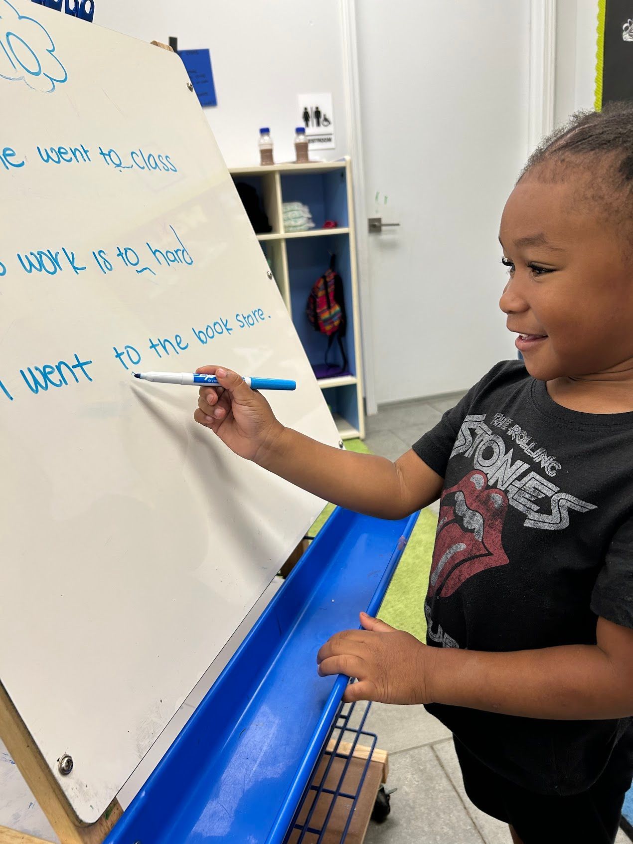 A young boy is writing on a whiteboard in a classroom.