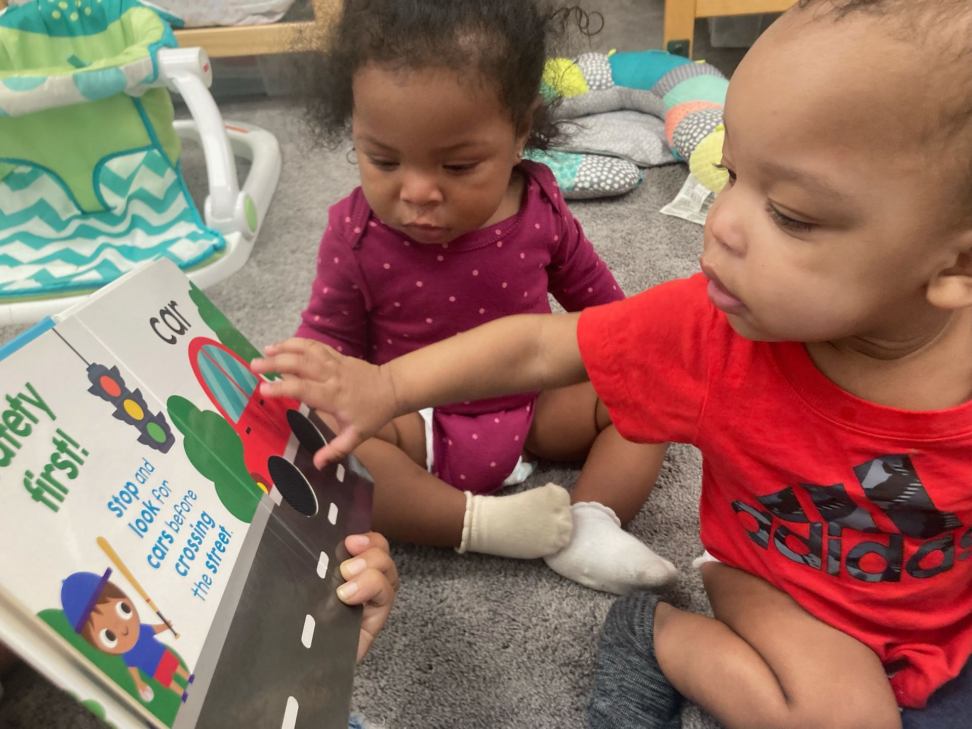 Two children are sitting on the floor drawing on a large piece of paper.