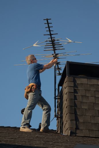 A Man Is Standing on A Roof Fixing an Antenna — A1 Antenna Doctor In Laurieton, NSW