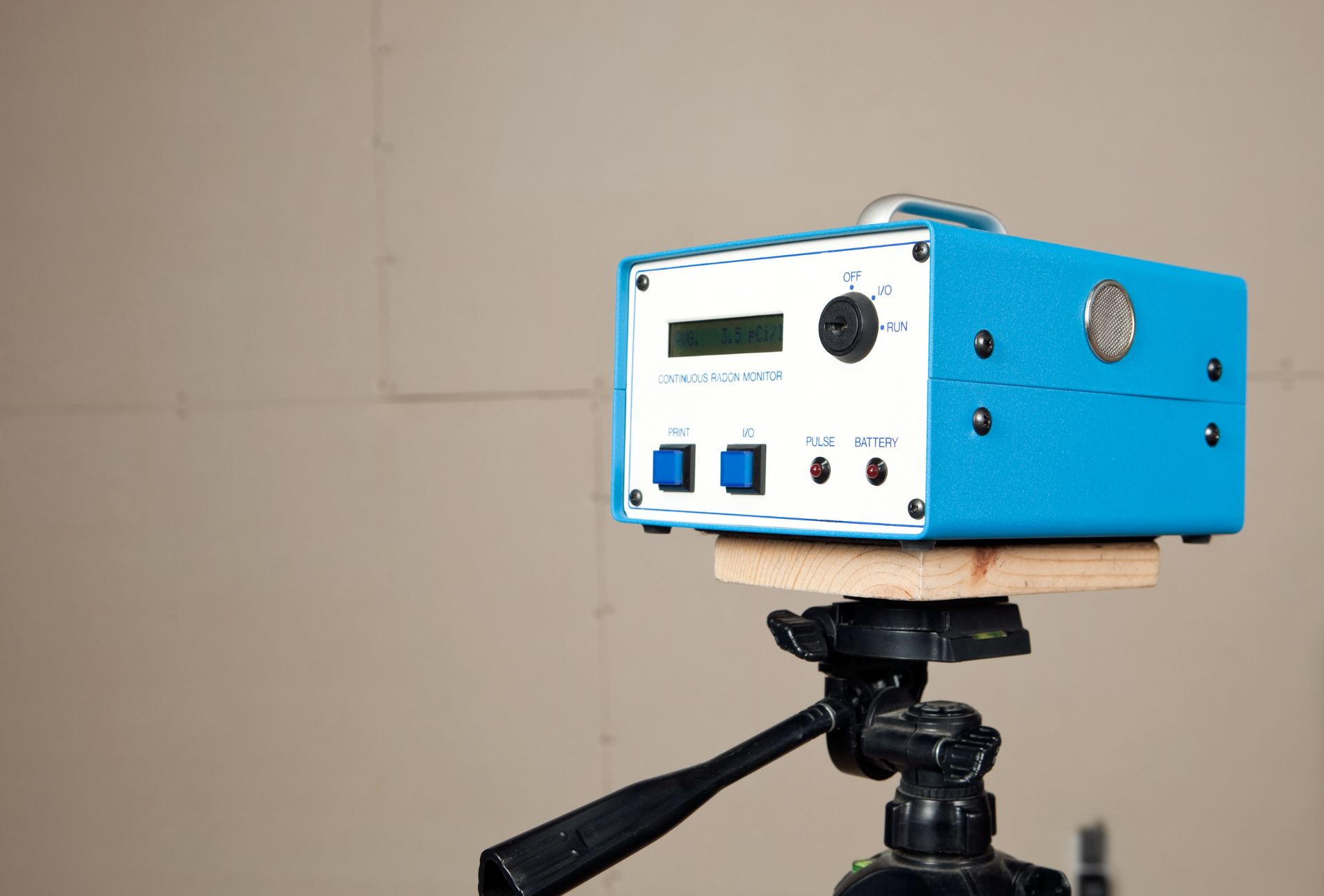 Blue electronic device on a tripod. The device has buttons, a knob, and a screen. Light tan background.