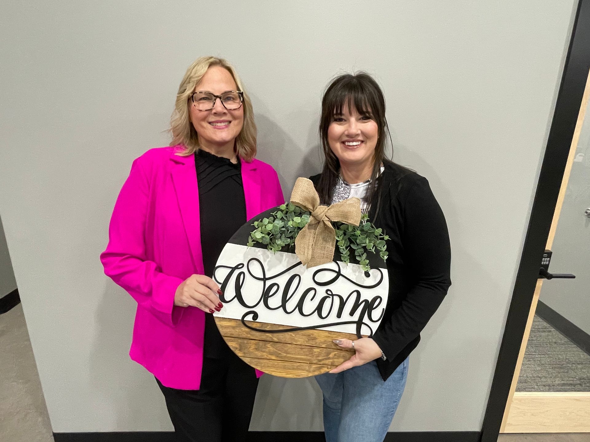 Two people smile while holding a circular wooden 