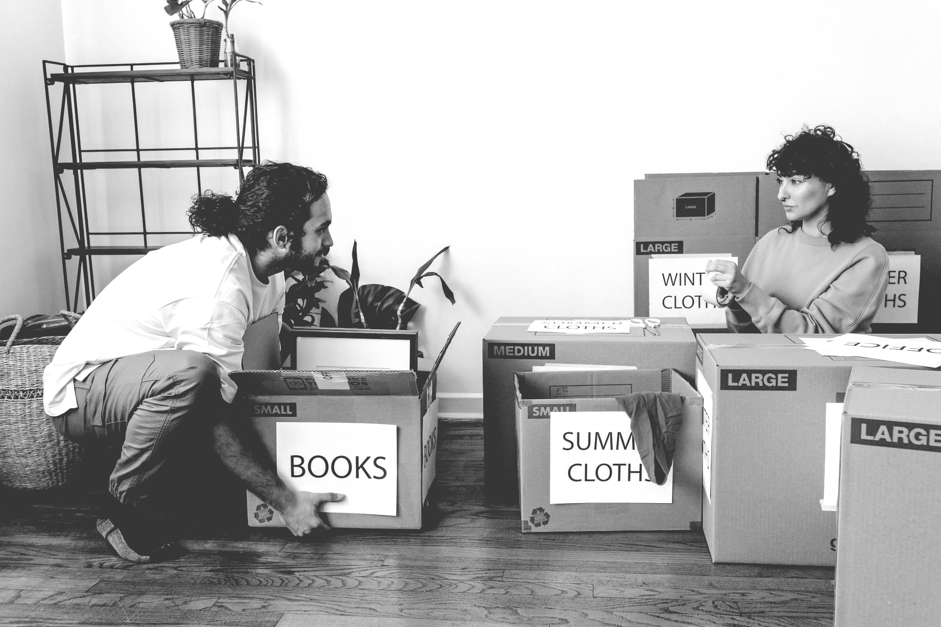 Two people in a bright room packing labeled cardboard boxes for a move.