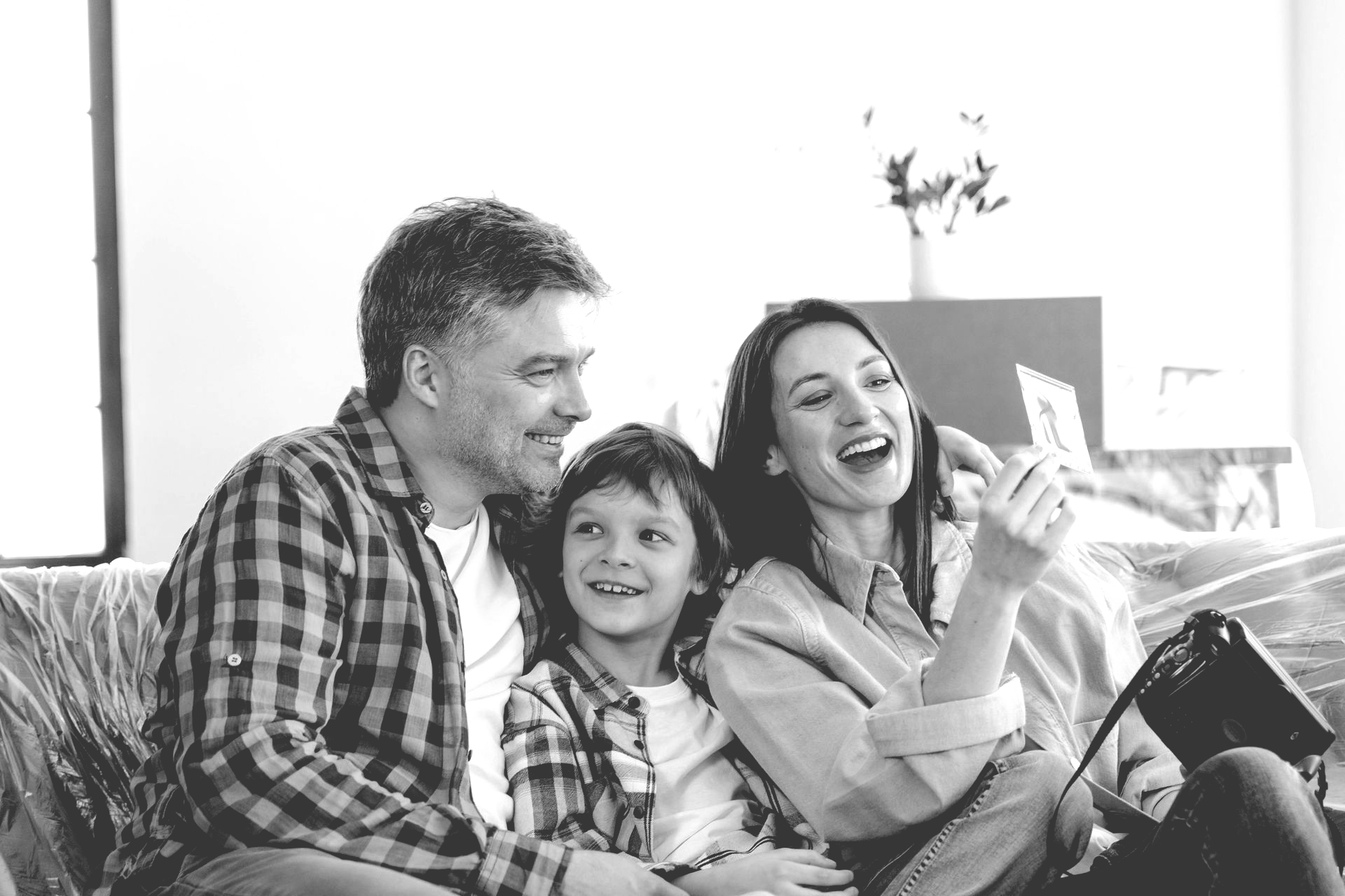 A family sits together indoors, smiling while looking at a small photograph held by the woman.