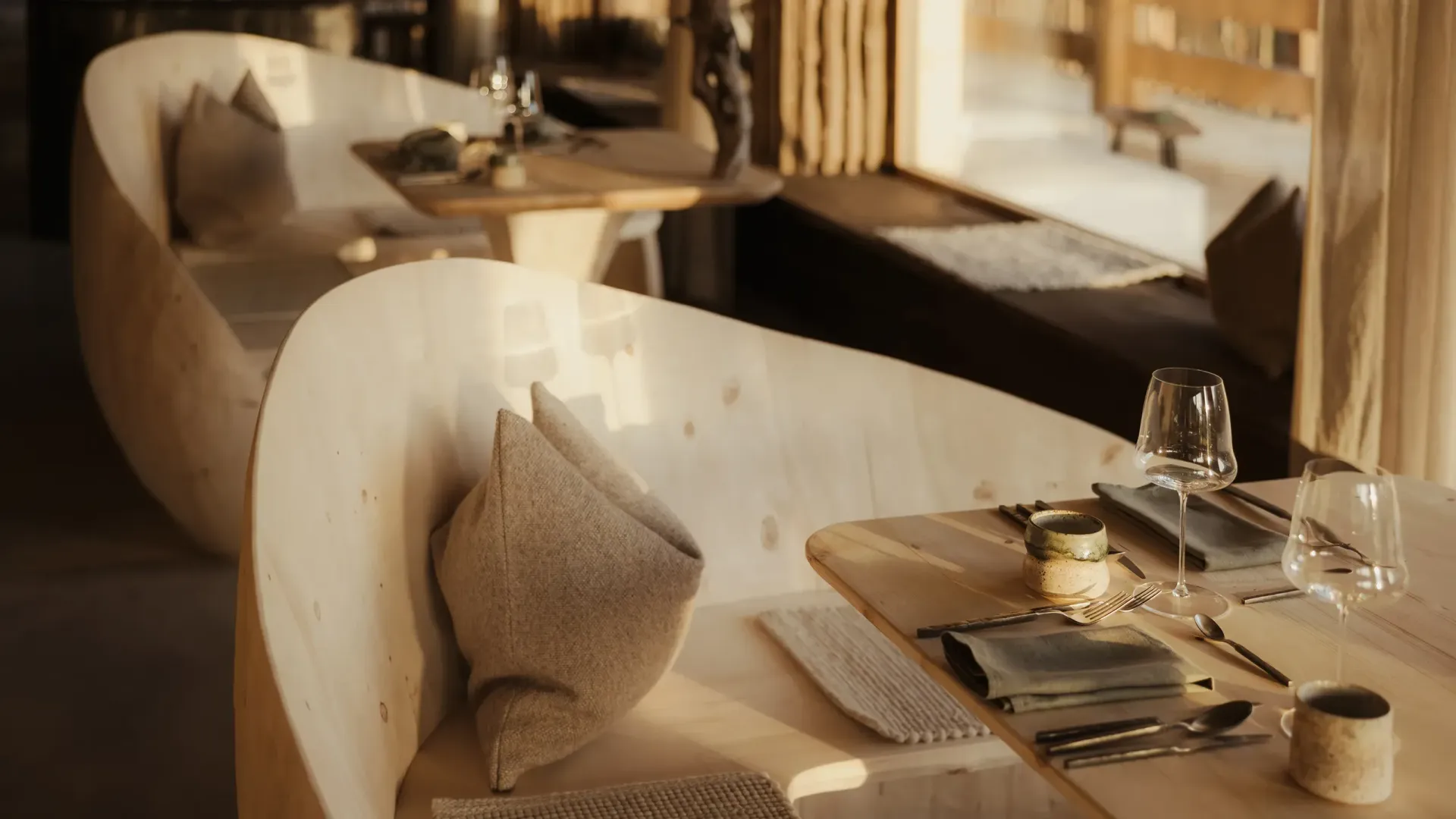 A cozy restaurant interior with curved, light wood booths and tables set with cutlery, napkins, and glassware.