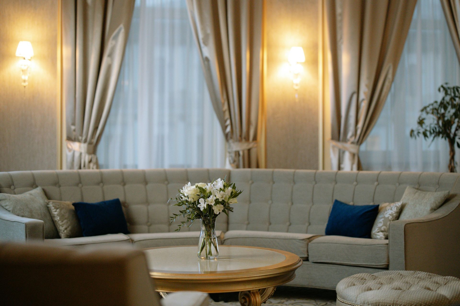 A tufted, curved beige sofa with blue accent pillows and a central flower bouquet in a warmly lit, elegant room.