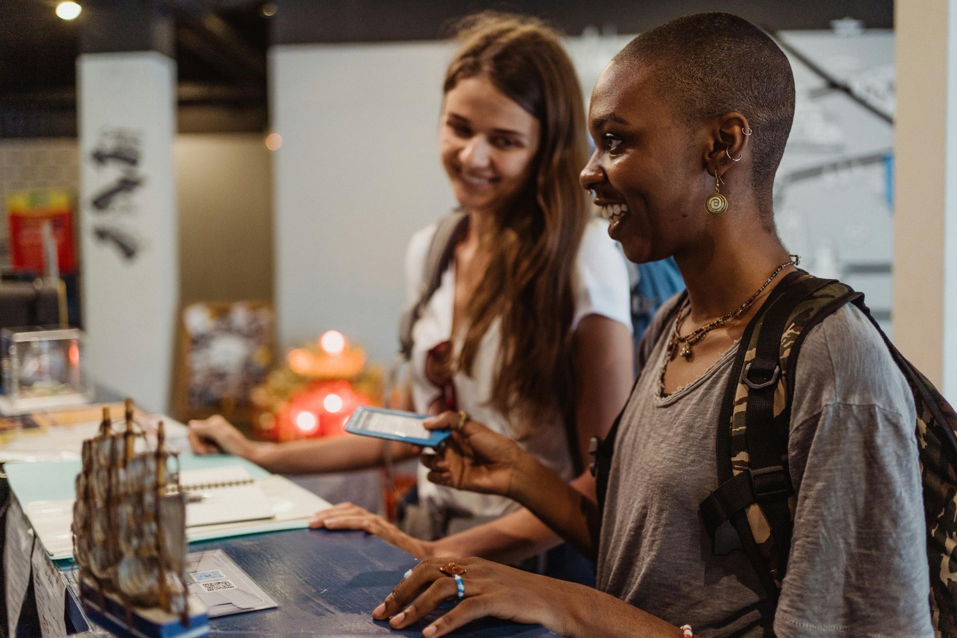Two people stand at a counter in an indoor space, looking at a small item held in a hand while smiling.