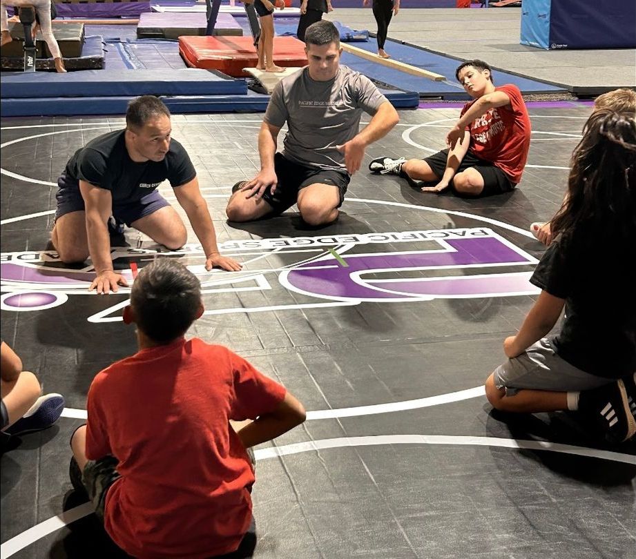 A group of people are sitting on the floor of a gym.