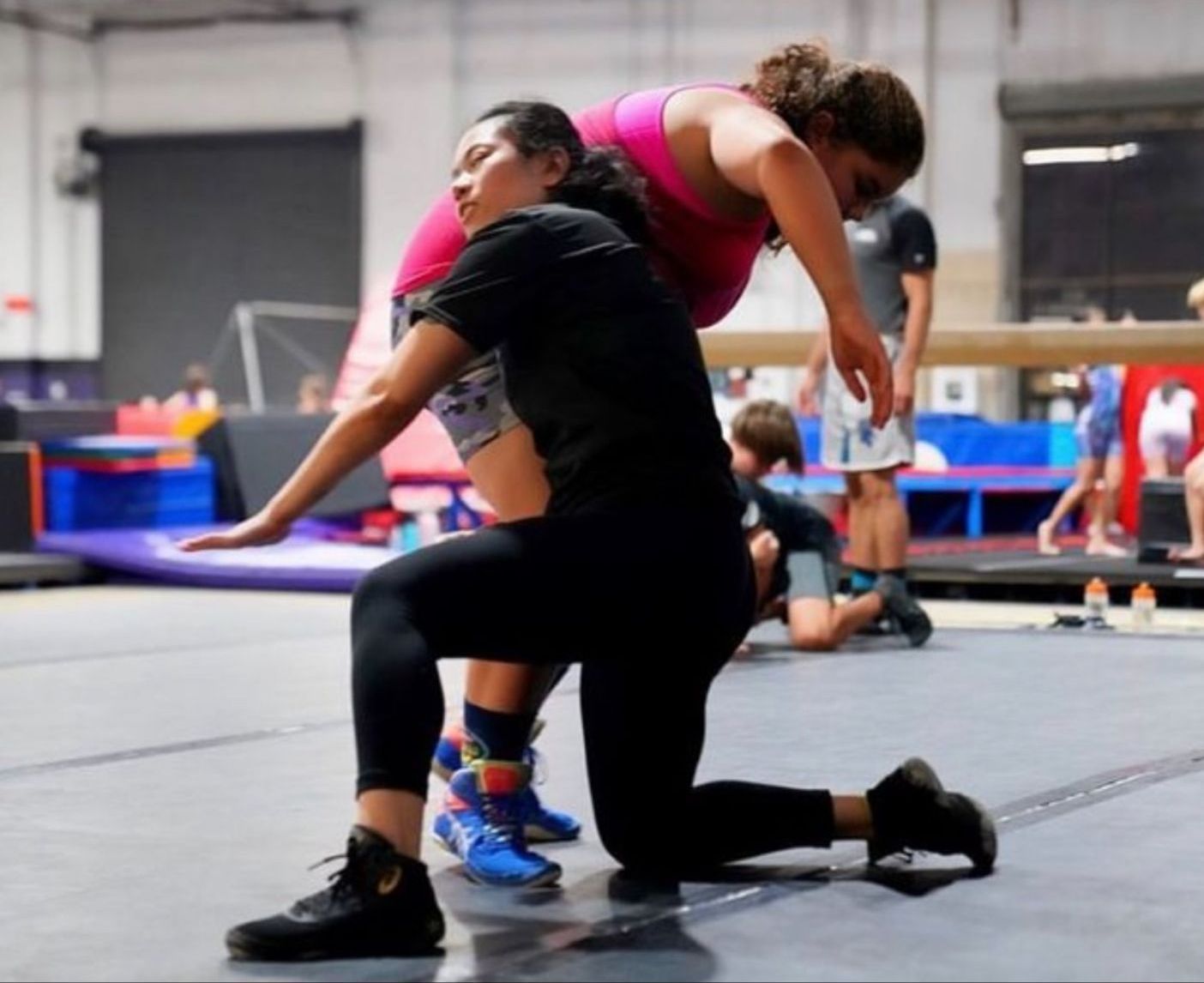 A woman in a pink tank top is helping another woman on her knees