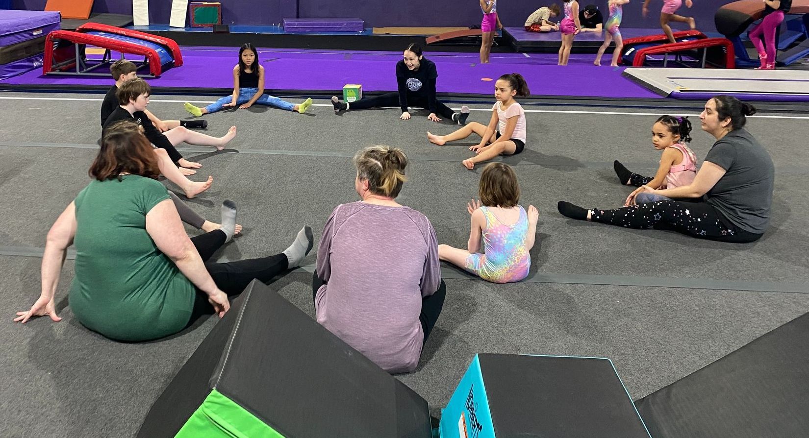 A group of people are sitting in a circle on the floor in a gym.