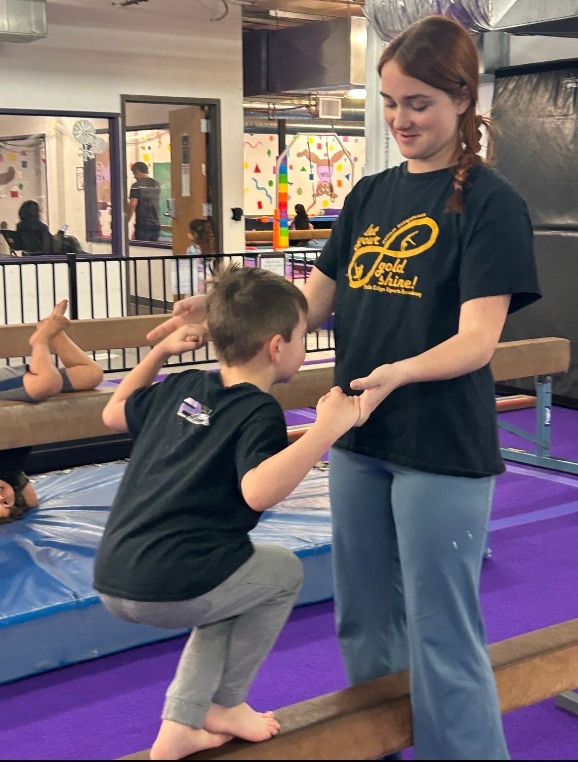 A woman is helping a young boy balance on a balance beam