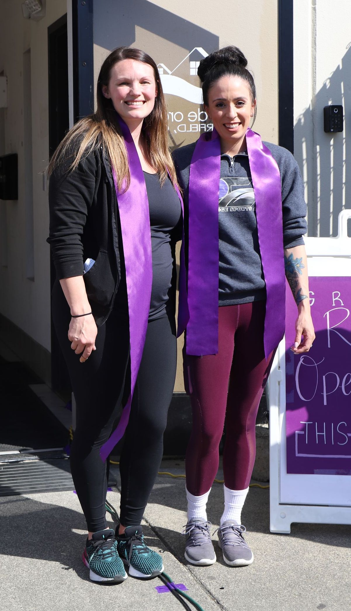 Two women wearing purple sashes are posing for a picture.
