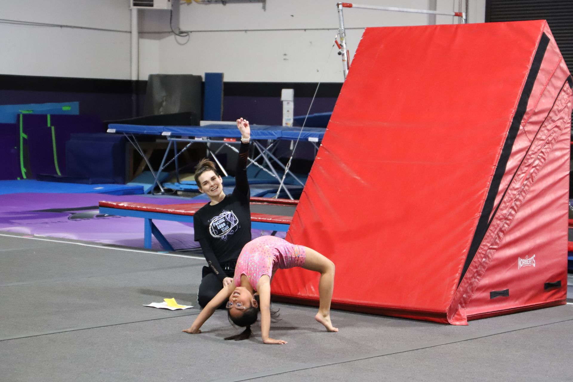 A young girl is sitting on a balance beam in a gym.