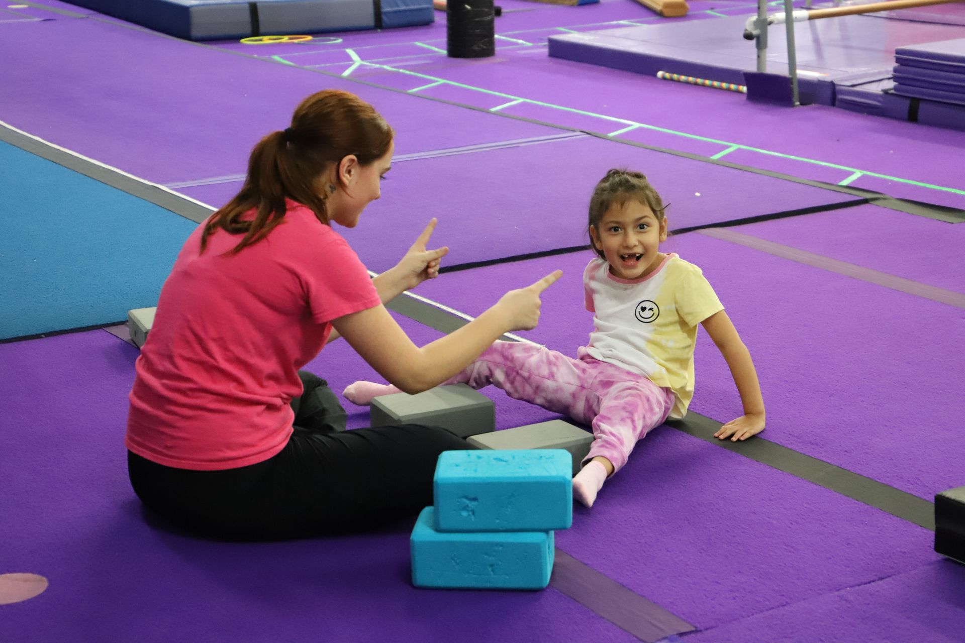 A group of people are sitting in a circle on the floor in a gym.