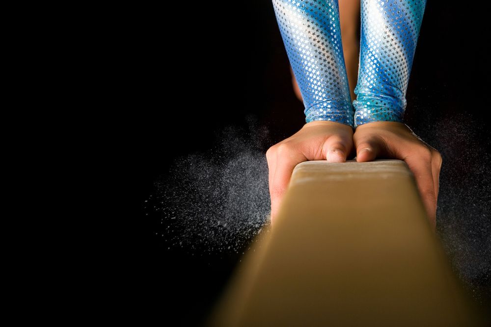 A gymnast is sitting on a balance beam covered in chalk.