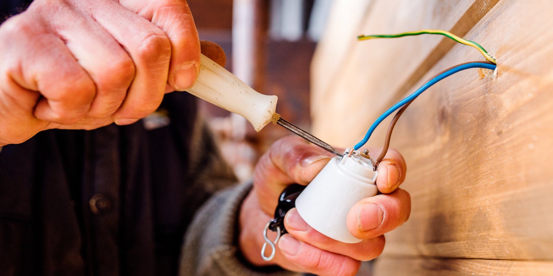 Person using a screwdriver to attach wires to a light fixture.