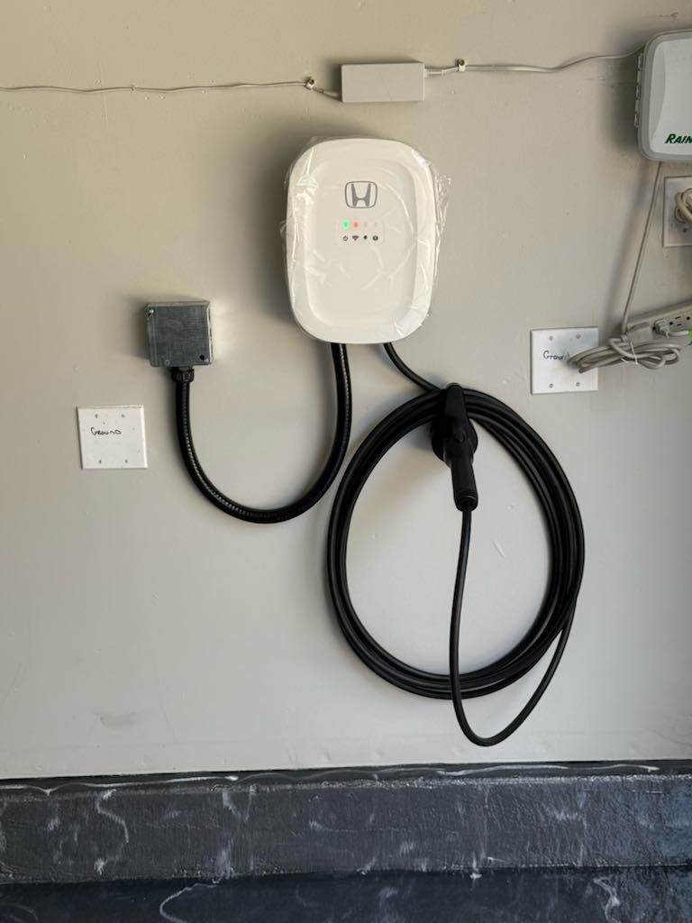 White EV charger mounted on a gray wall, with a black cable and connector.