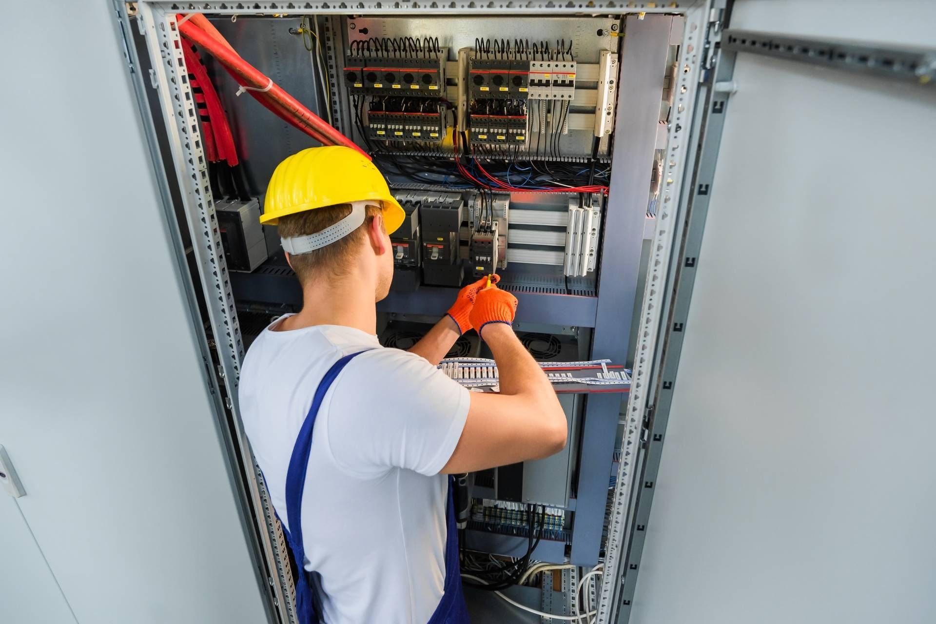 Electrician in yellow hard hat and orange gloves working inside an electrical panel.