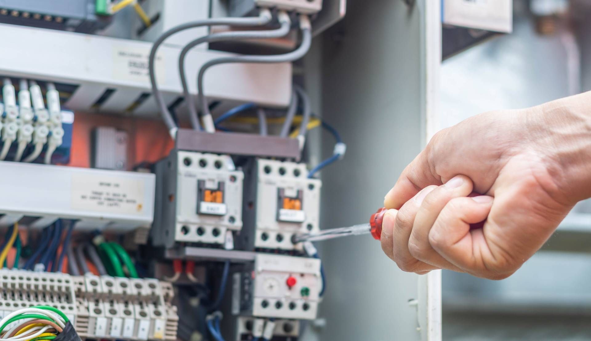 Person using screwdriver on electrical panel, wires and components visible.