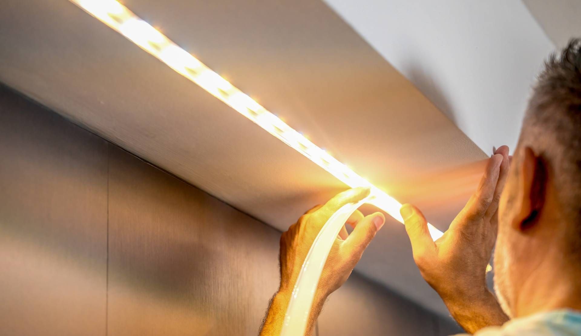 Person installing warm-toned LED strip lights on a wall.