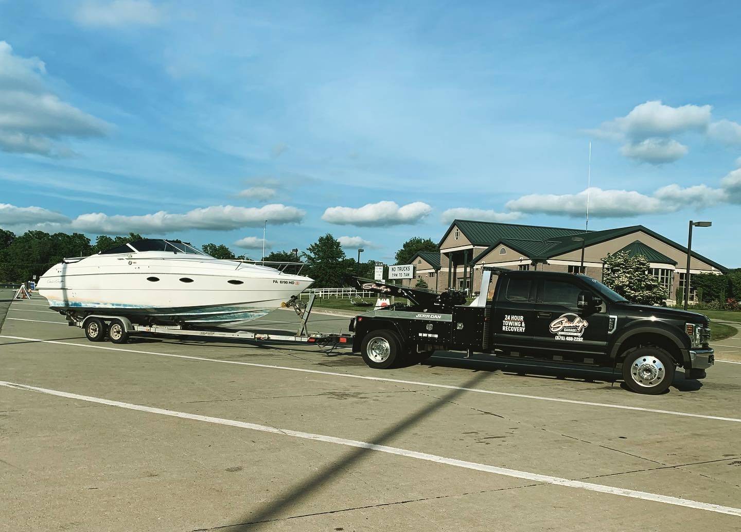 Black tow truck towing a white boat on a trailer on a paved road under a blue sky.