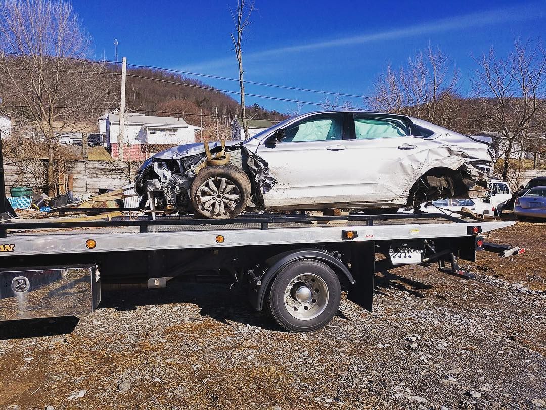 A badly damaged white car on a tow truck.