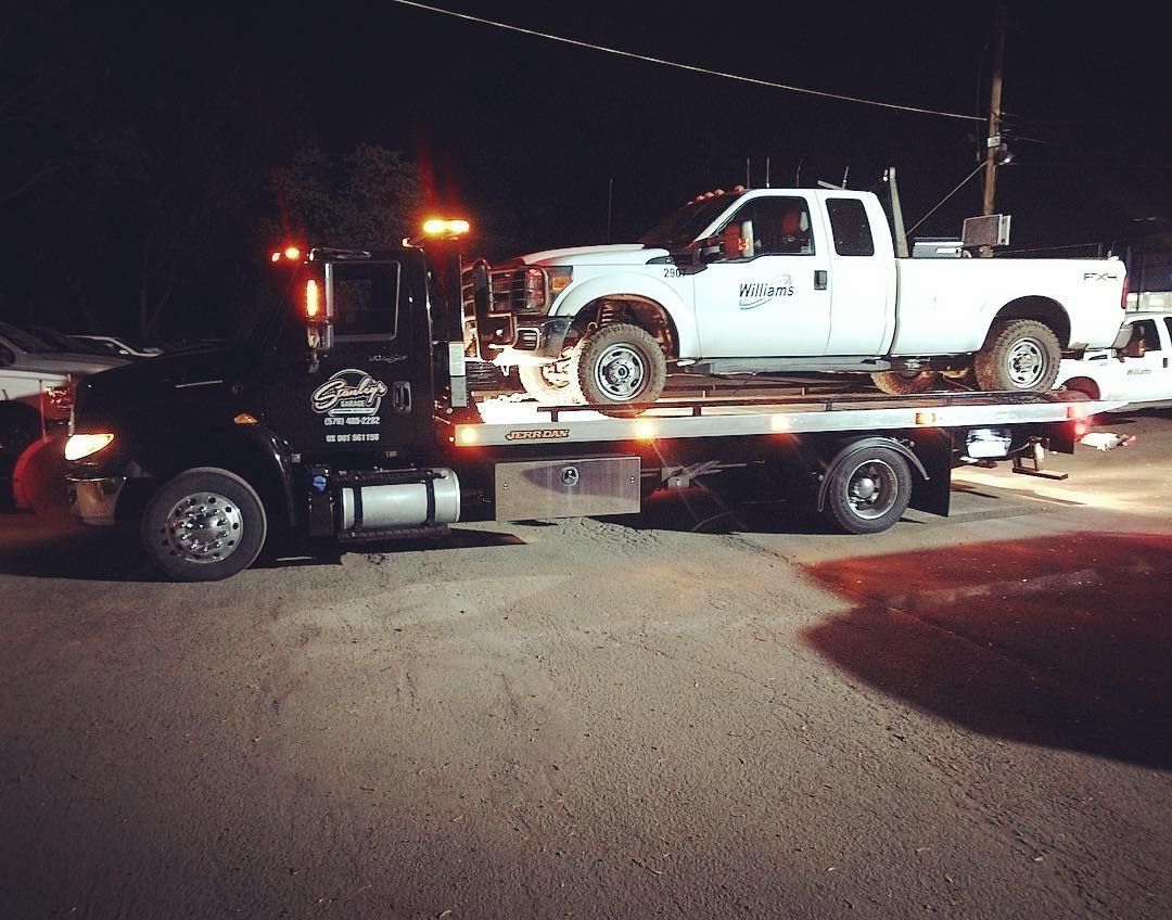 Black tow truck carrying a white pickup truck at night.