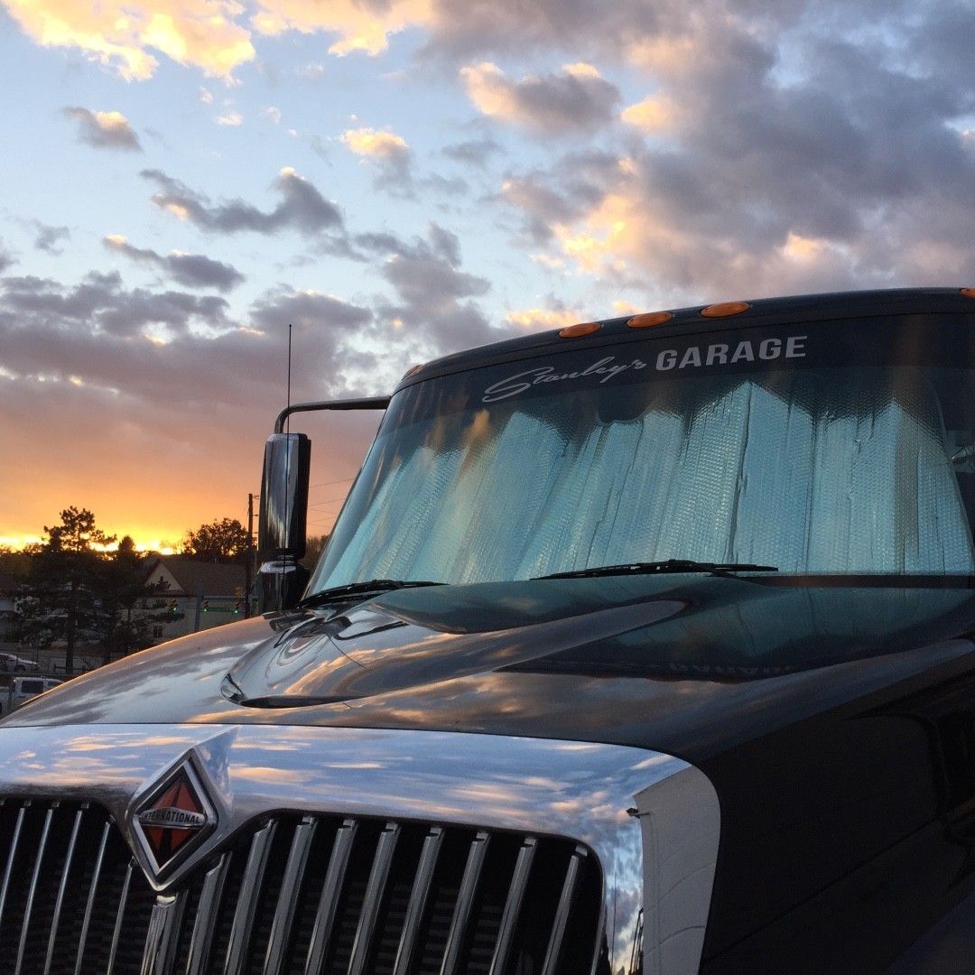 Semi-truck at sunset, windshield shade up. Garage logo visible on top. Silver, black, and orange hues.