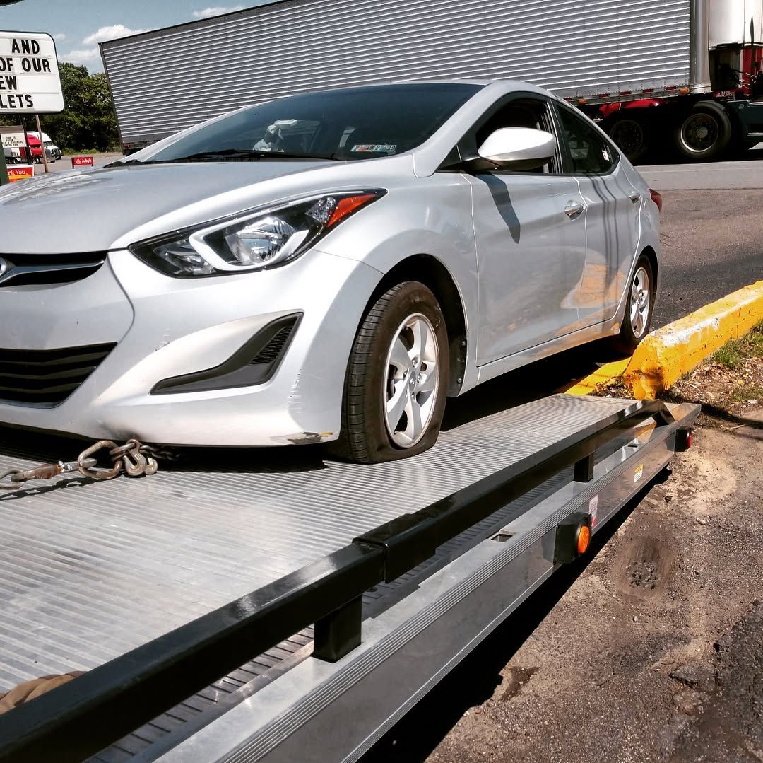 Silver Hyundai Elantra on a tow truck. The car has a flat tire, parked near a curb.