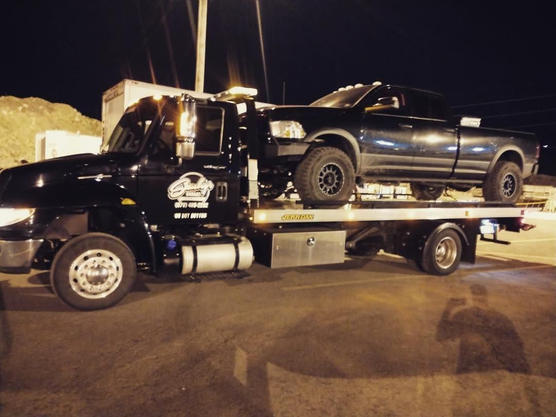 Black tow truck carrying a black pickup truck on its flatbed at night.