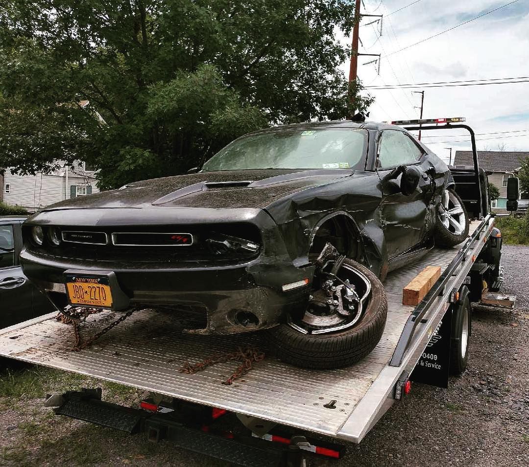 Dark gray Dodge Challenger on a tow truck, front end damaged.