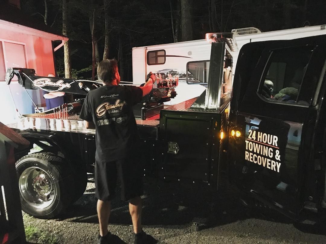 Tow truck at night, loading a camper; two people involved; emergency lights visible.
