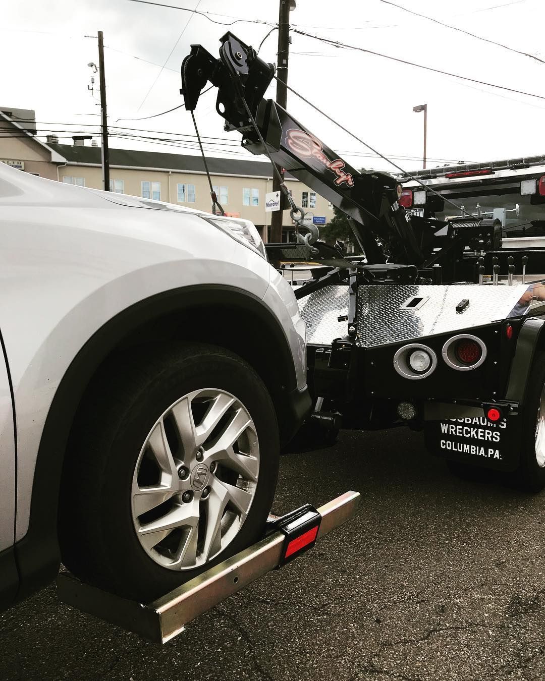 White car being towed by a black tow truck; car wheel on a towing dolly.