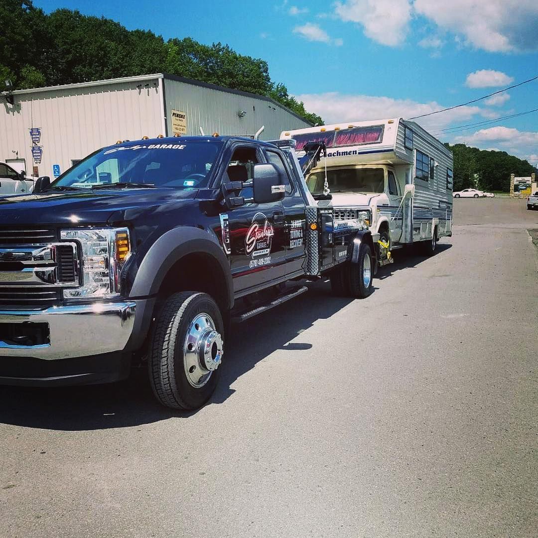 Black tow truck towing a white RV in a parking lot on a sunny day.