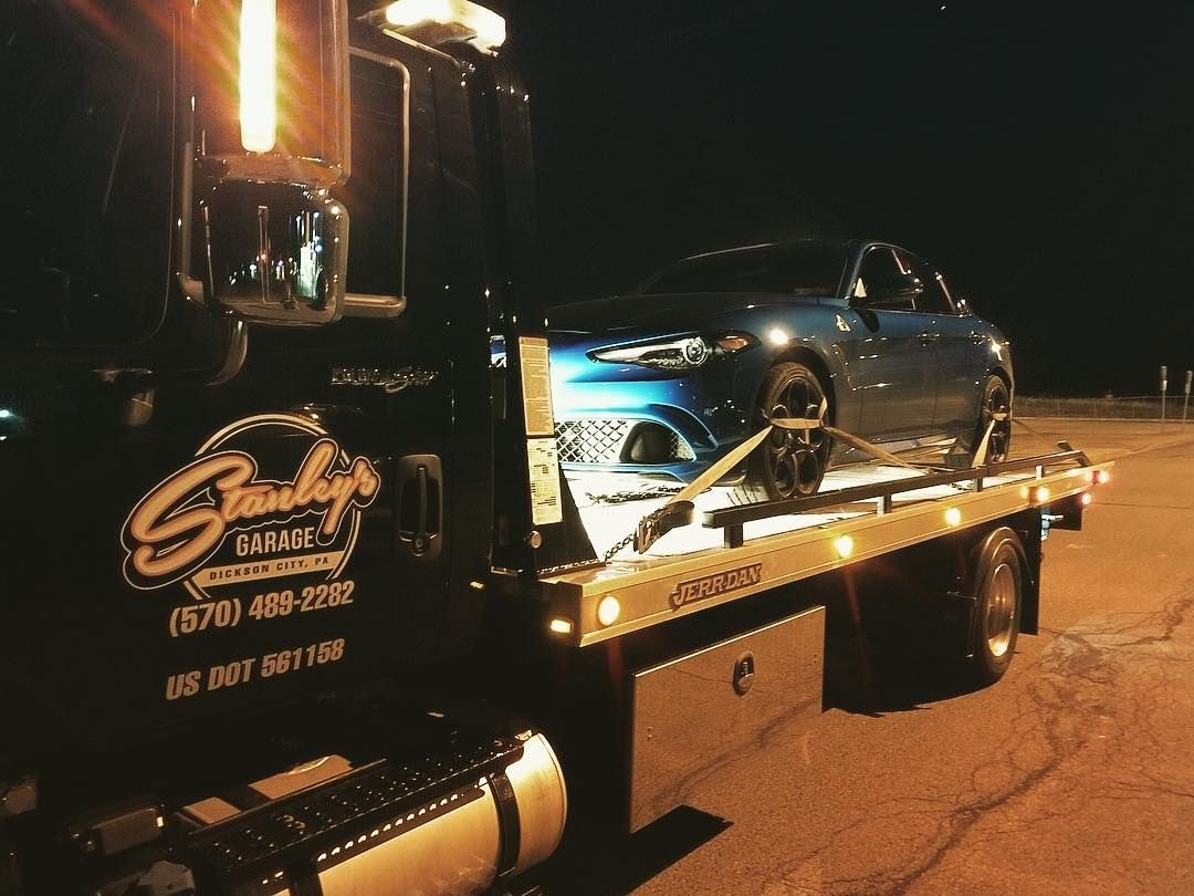 Blue car being towed onto a flatbed tow truck at night. 