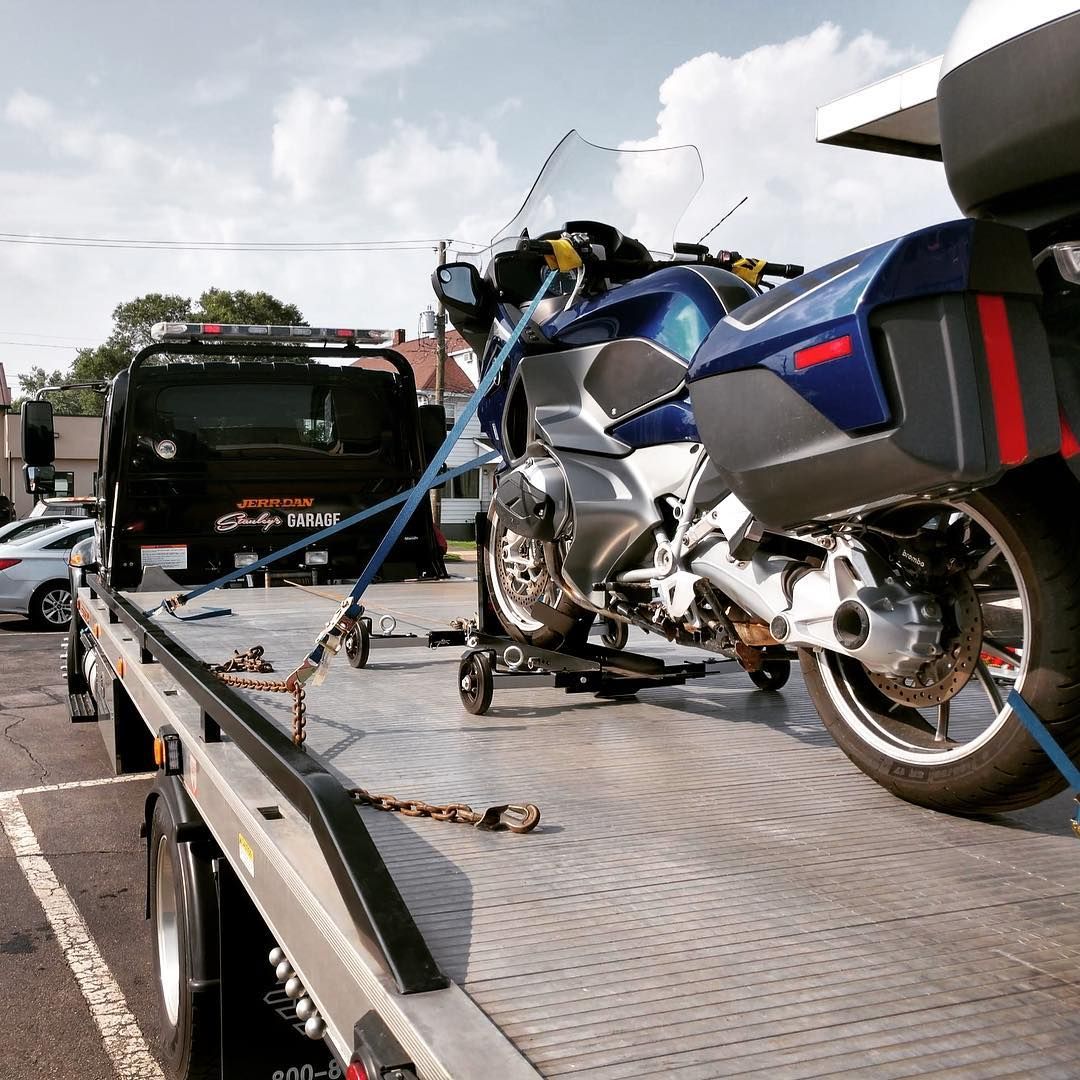 Blue motorcycle secured on the bed of a tow truck in an outdoor setting.