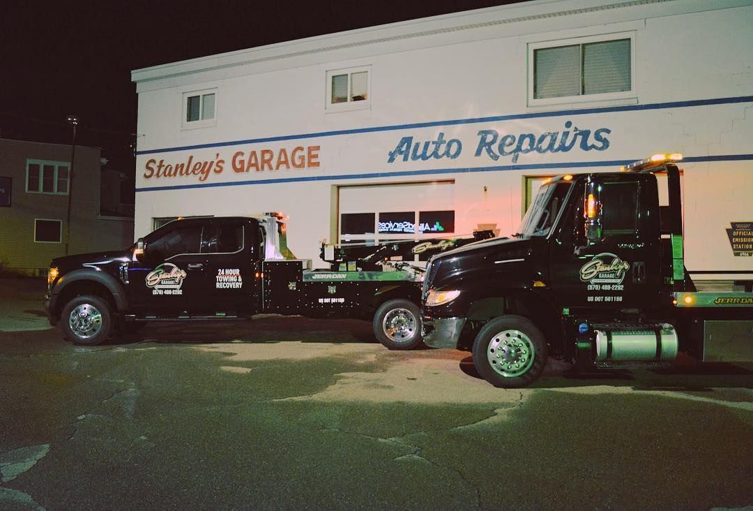 Two black tow trucks parked in front of Stanley's Garage at night. The building is white with red and blue lettering.