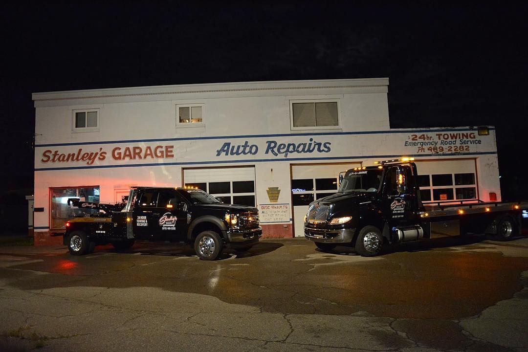 Two tow trucks outside Stanley's Garage at night, building sign says 