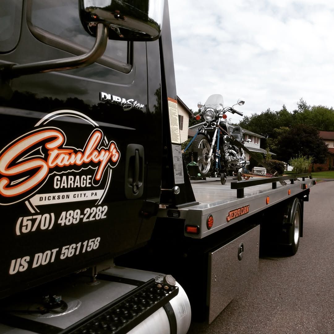 Black tow truck with motorcycle on flatbed, parked on a street. 