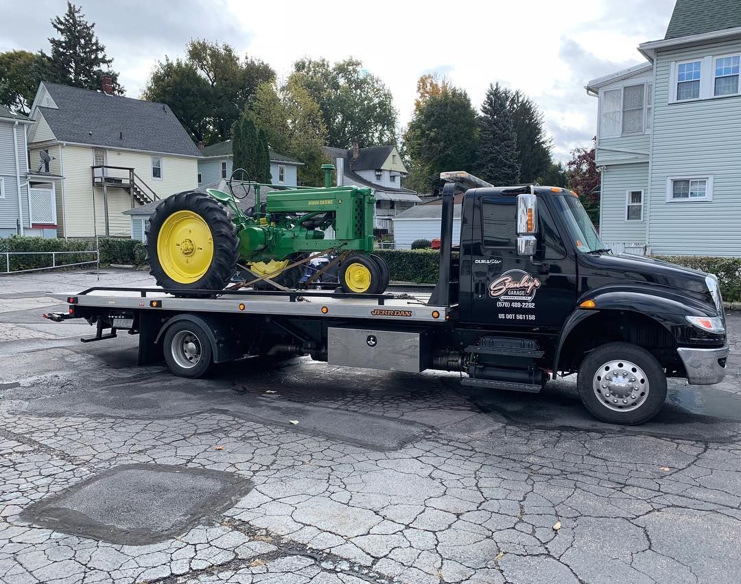 John Deere tractor on a black tow truck in a parking lot.